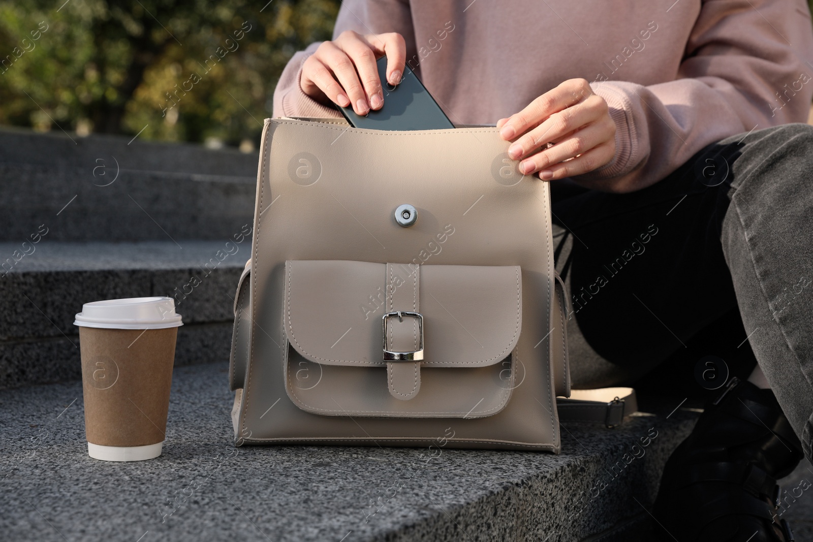 Photo of Woman putting smartphone into stylish beige backpack on stairs outdoors, closeup