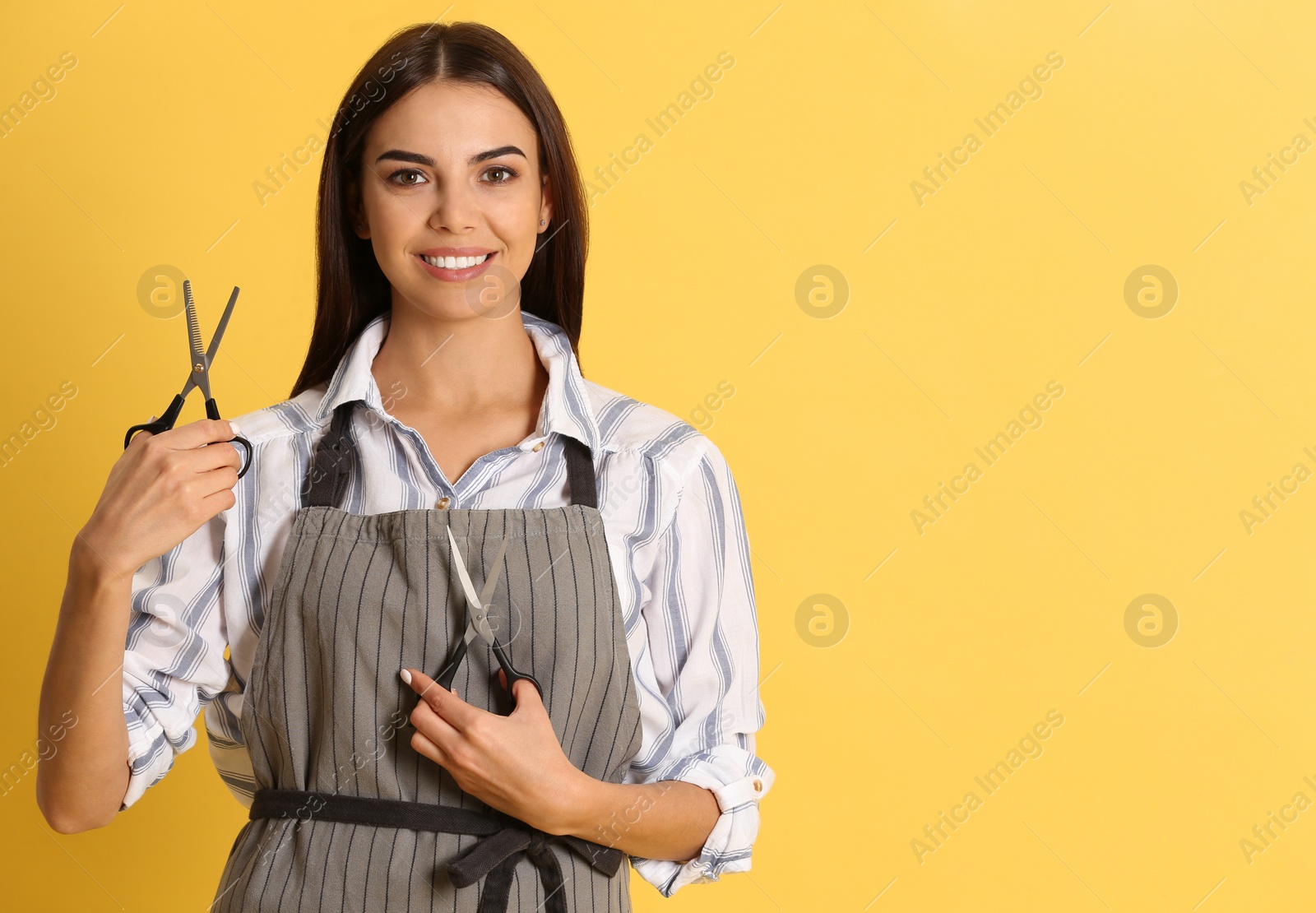 Photo of Young hairstylist holding professional scissors on color background, space for text