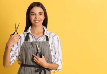 Young hairstylist holding professional scissors on color background, space for text