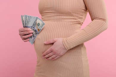 Surrogate mother. Pregnant woman with dollar banknotes on pink background, closeup