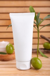 Tube of natural cream, olives and leaves on wooden table