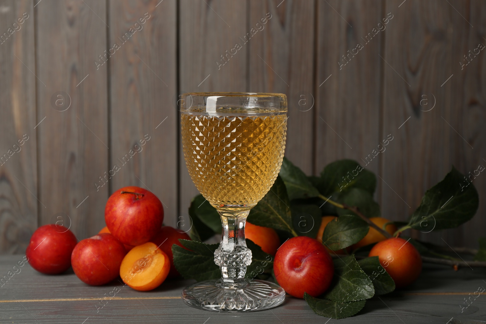 Photo of Delicious plum liquor and ripe fruits on grey wooden table. Homemade strong alcoholic beverage