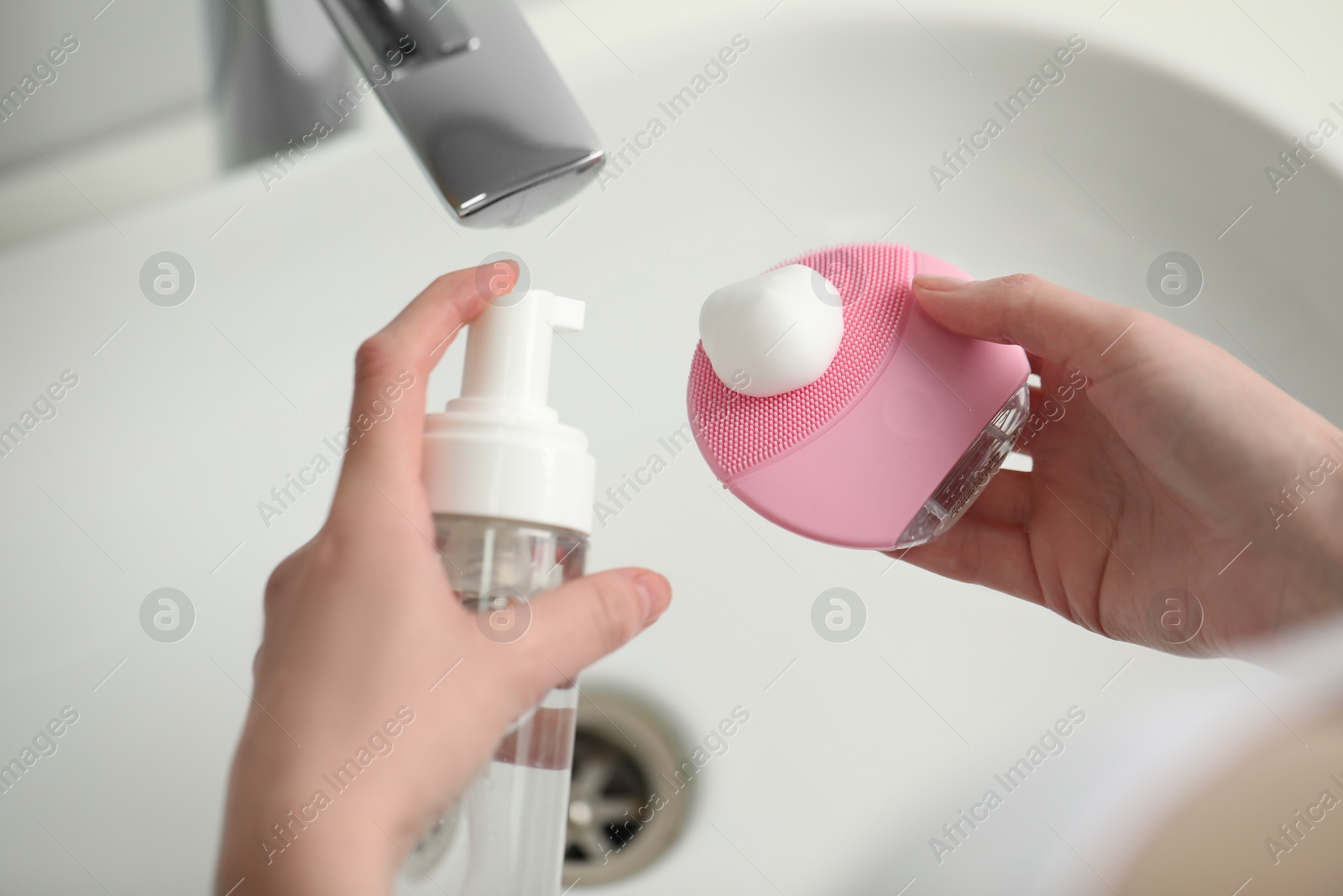 Photo of Washing face. Woman applying cleansing foam onto brush above sink in bathroom, closeup