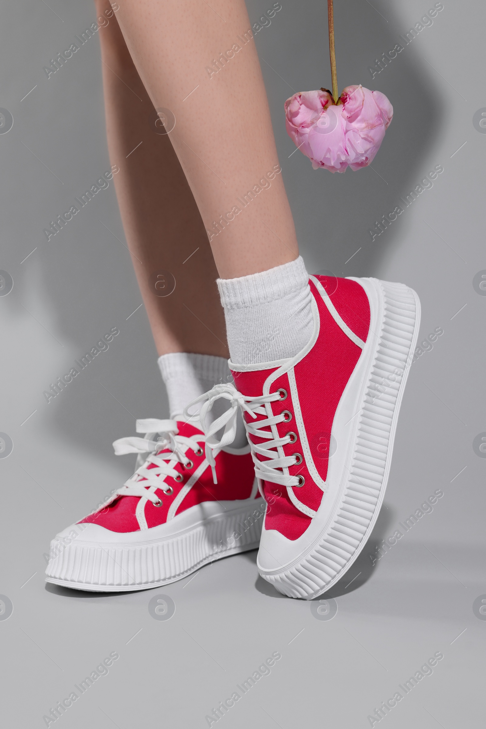 Photo of Woman posing in red classic old school sneakers with beautiful flower on light gray background, closeup