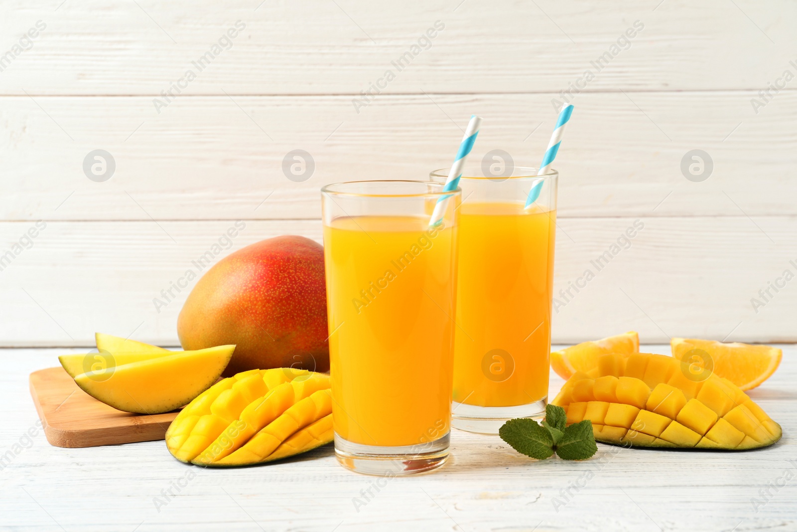 Photo of Tasty mango drink and fresh fruits on wooden table against light background