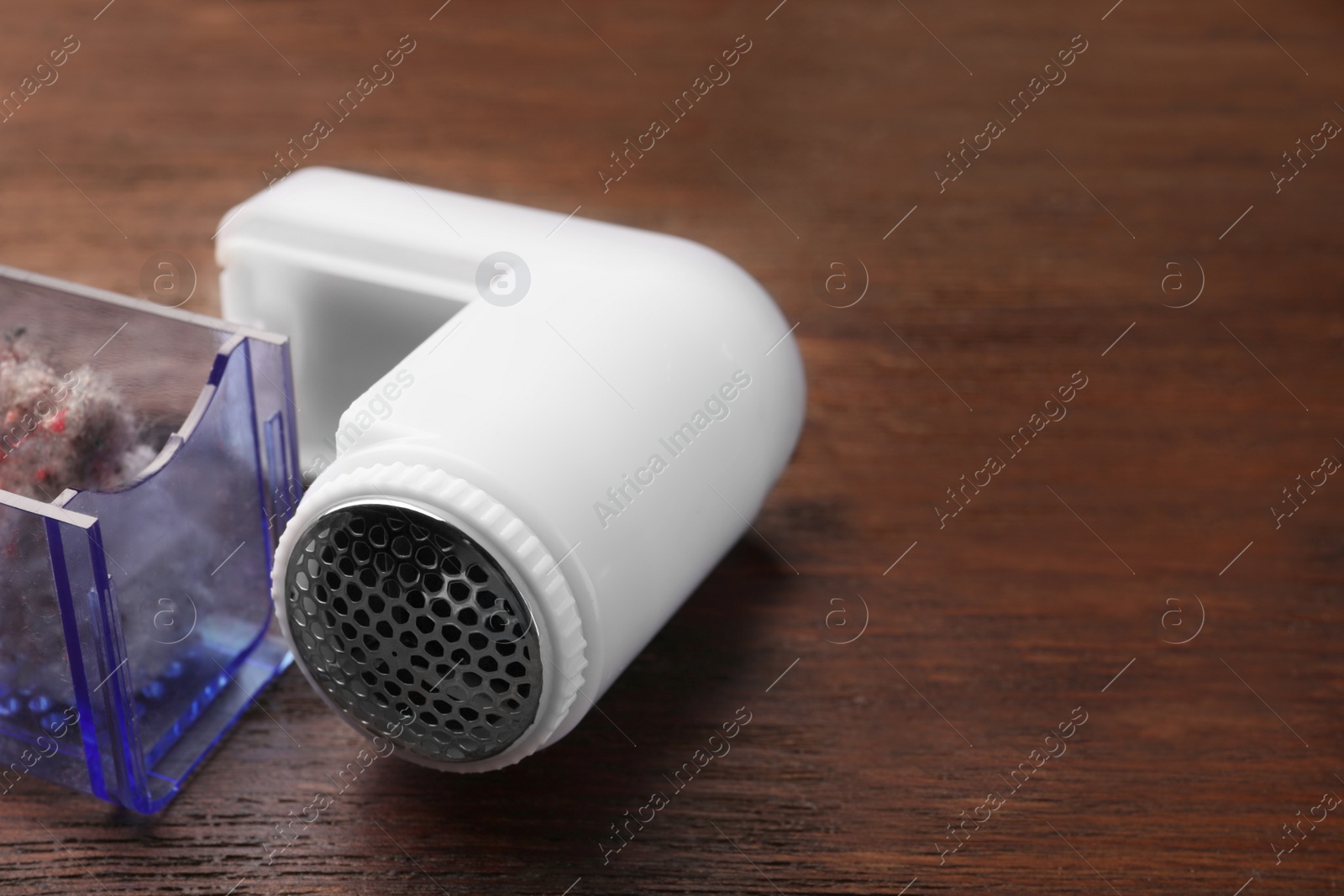 Photo of Modern fabric shaver with fuzz on wooden table, closeup. Space for text