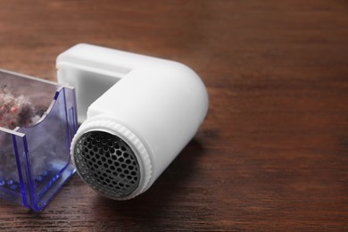 Photo of Modern fabric shaver with fuzz on wooden table, closeup. Space for text