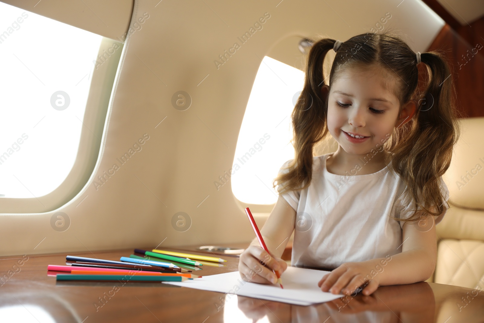 Photo of Cute little girl drawing at table in airplane during flight