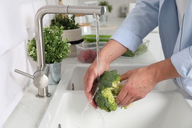 Man washing fresh broccoli in kitchen, closeup. Food storage