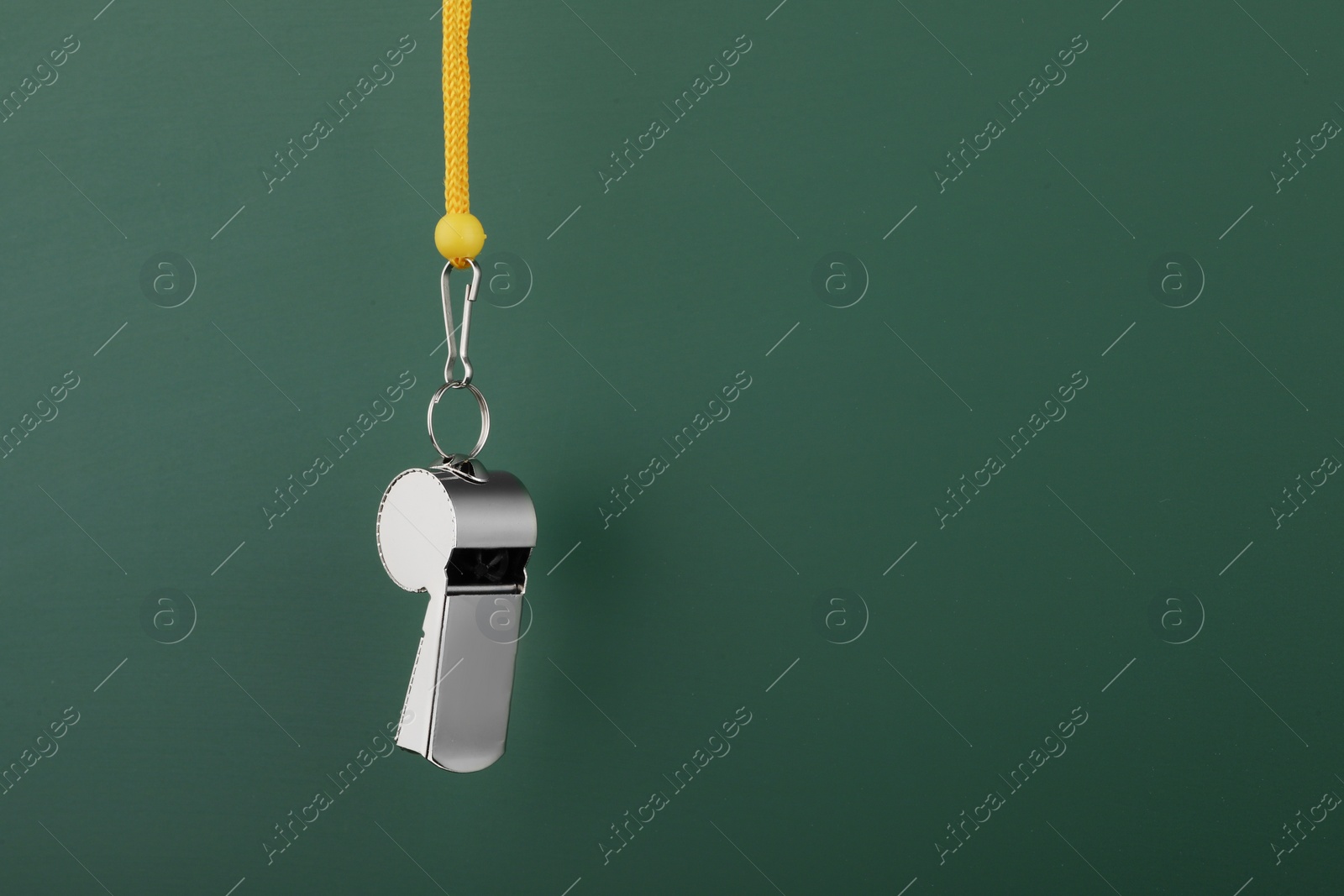 Photo of Referee equipment. Metal whistle on dark green background, closeup and space for text