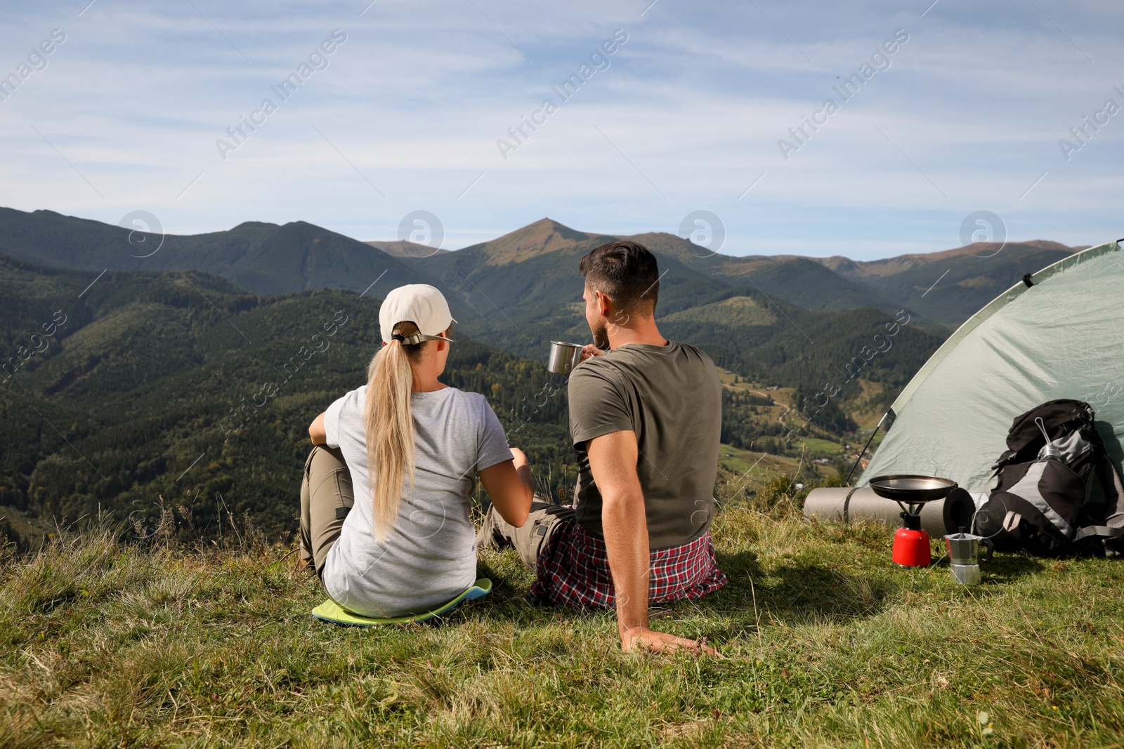 Photo of Couple enjoying mountain landscape near camping tent, back view