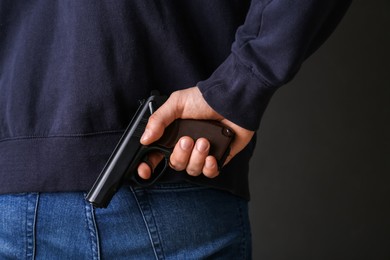 Photo of Man hiding gun behind his back on dark background, closeup