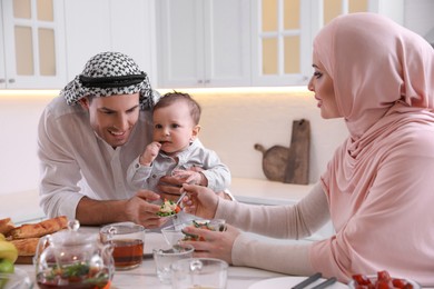 Happy Muslim family with little son at served table in kitchen