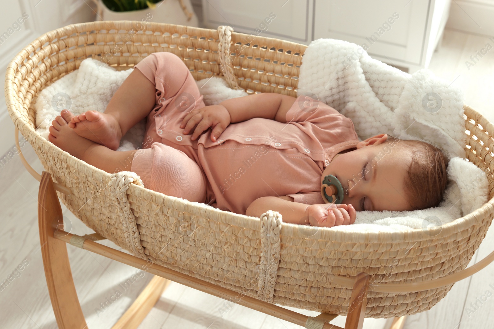 Photo of Cute little baby with pacifier sleeping in wicker crib at home