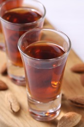 Photo of Shot glasses with tasty amaretto liqueur and almonds on wooden board, closeup