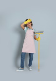 Photo of Tired African American woman with yellow broom on grey background