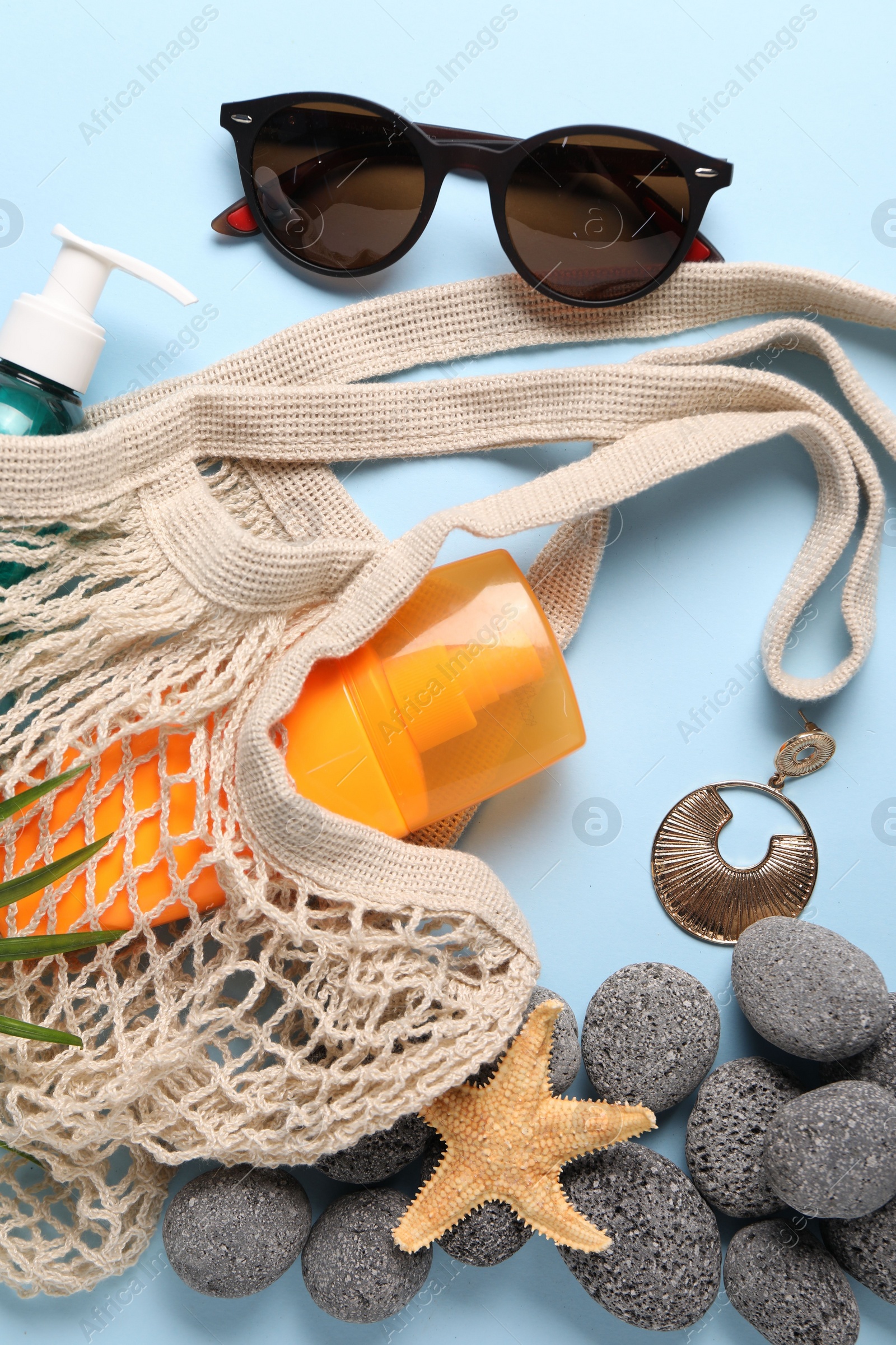 Photo of String bag and different beach accessories on light blue background, flat lay