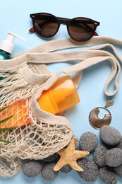 String bag and different beach accessories on light blue background, flat lay