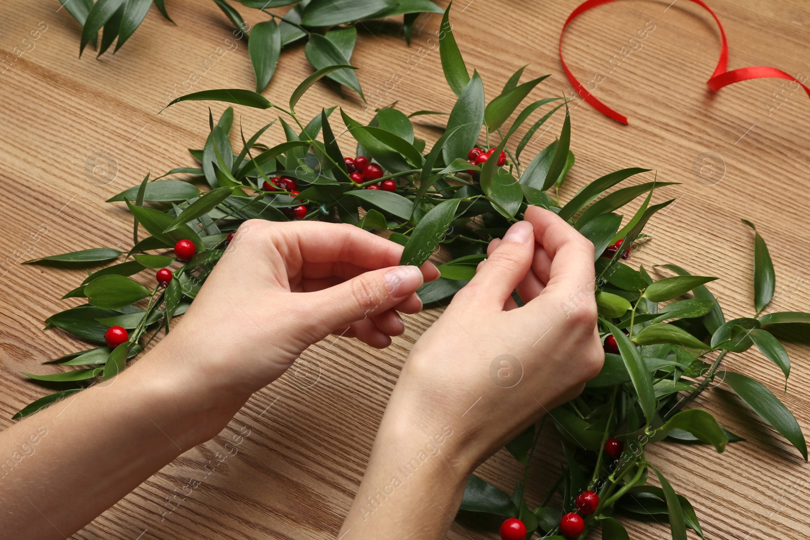 Photo of Woman making mistletoe wreath at wooden table, closeup. Traditional Christmas decor