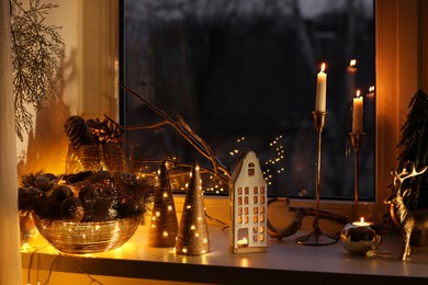 Many beautiful Christmas decorations, candlesticks and festive lights on window sill indoors