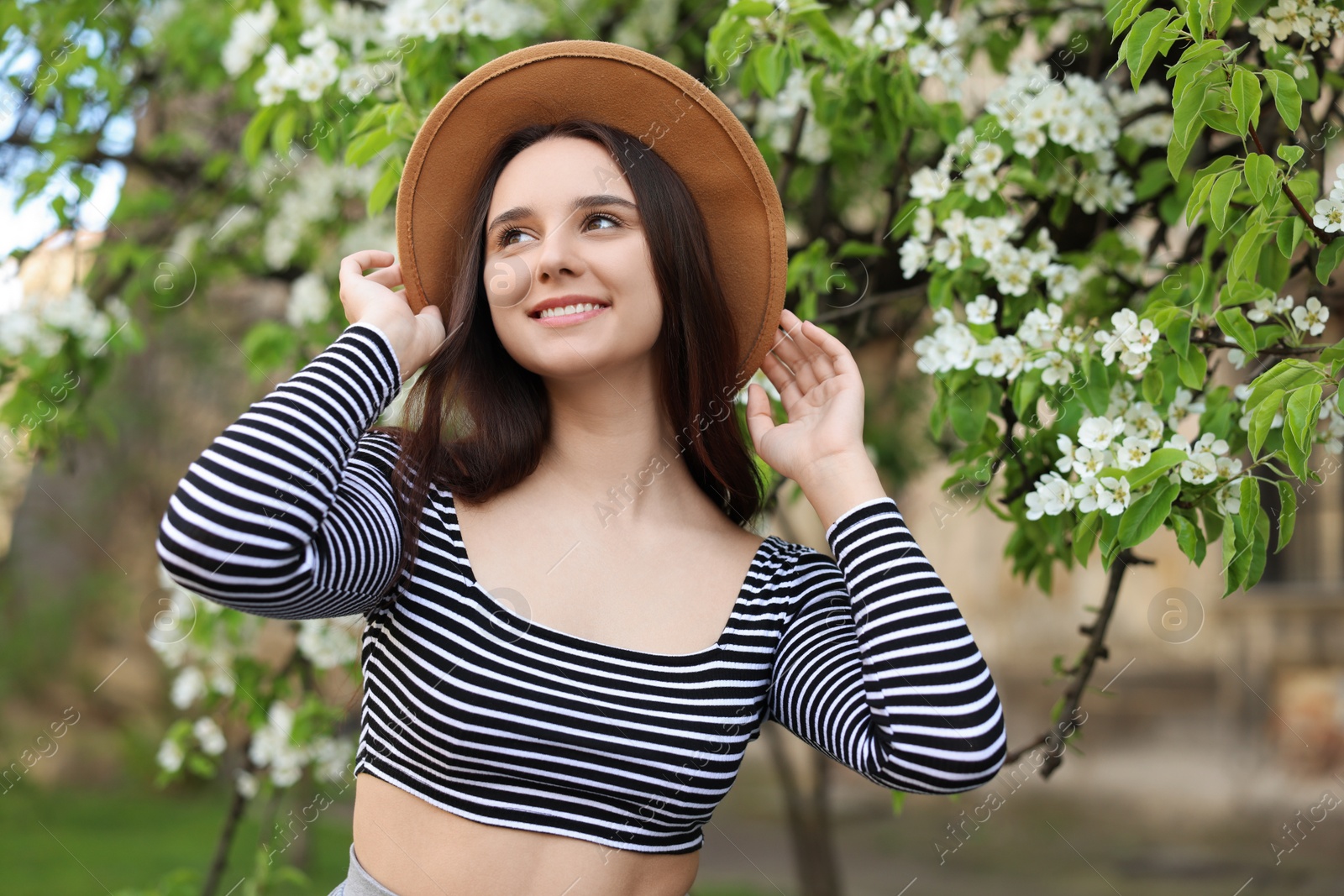 Photo of Beautiful woman in hat near blossoming tree on spring day