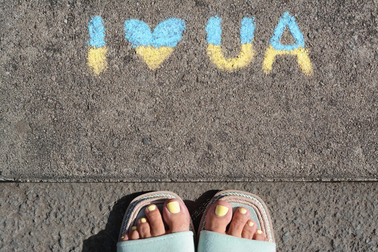 Photo of Woman near inscription I love Ukraine drawn by blue and yellow chalk on asphalt, top view