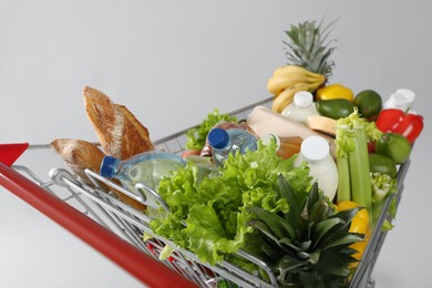 Photo of Shopping cart full of groceries on grey background, closeup