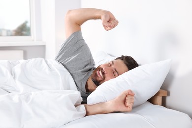 Happy man stretching on comfortable pillow in bed at home