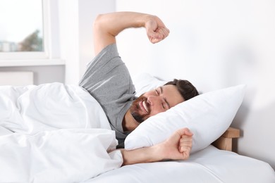 Photo of Happy man stretching on comfortable pillow in bed at home