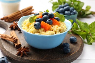 Photo of Tasty millet porridge with blueberries, pumpkin and mint in bowl on white table, closeup