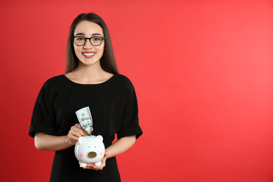 Photo of Young woman putting money into piggy bank on crimson background. Space for text