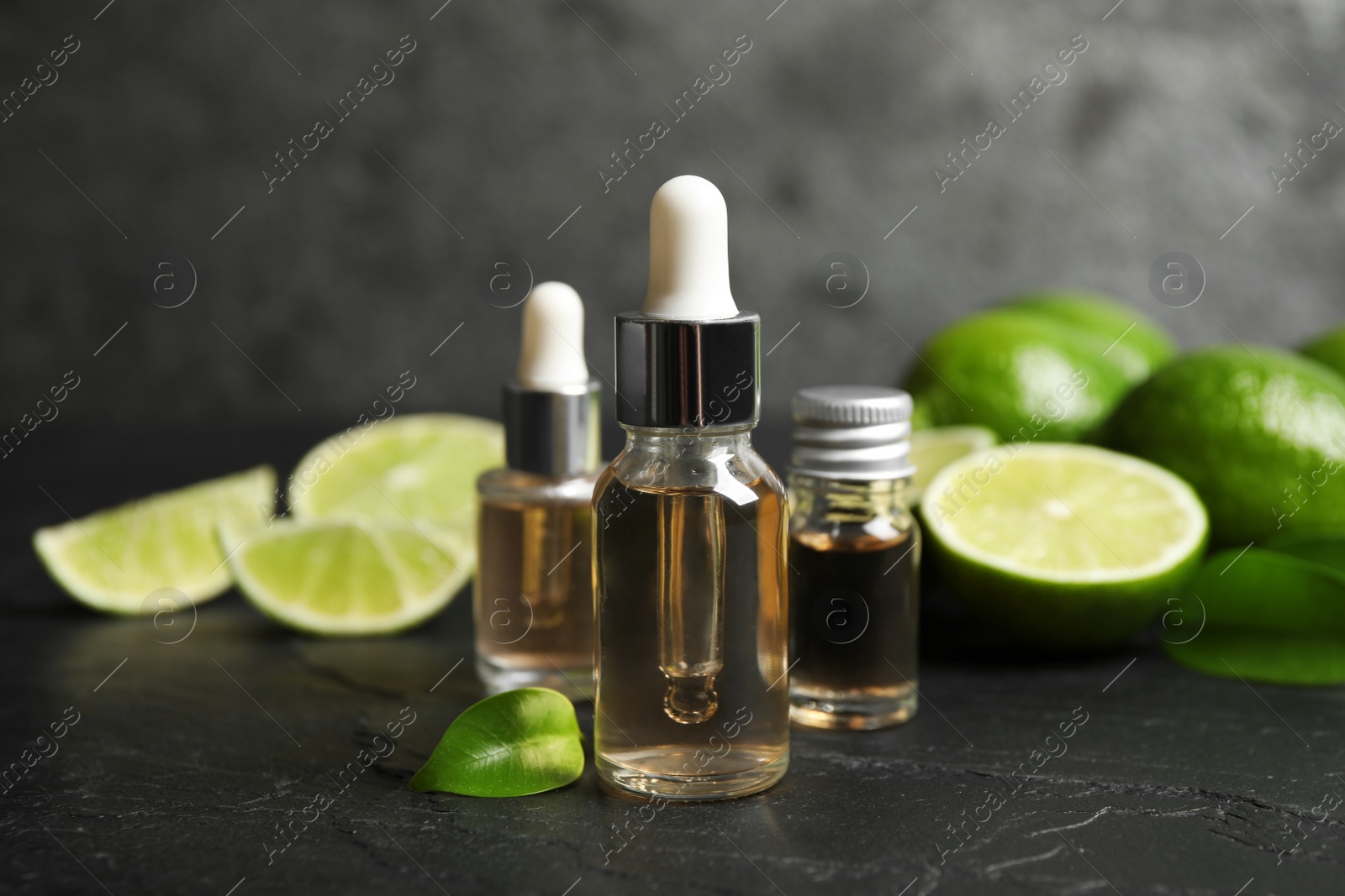 Photo of Lime essential oil and cut citrus fruits on black table