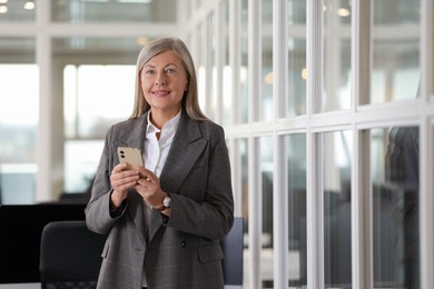 Smiling woman with smartphone in office, space for text. Lawyer, businesswoman, accountant or manager