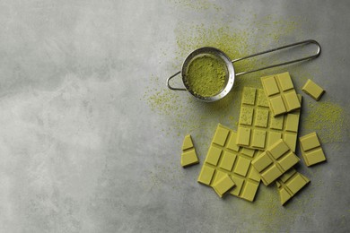 Pieces of tasty matcha chocolate bars and powder on grey textured table, flat lay. Space for text