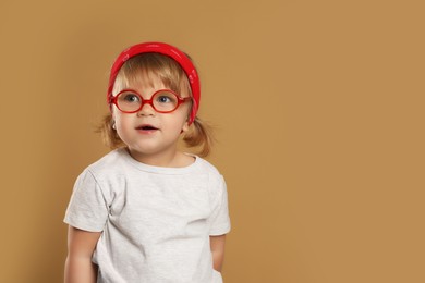 Cute little girl in glasses on pale brown background. Space for text