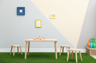 Stylish playroom interior with table, stools and green carpet