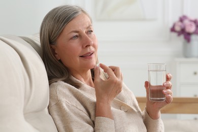 Senior woman with glass of water taking pill indoors