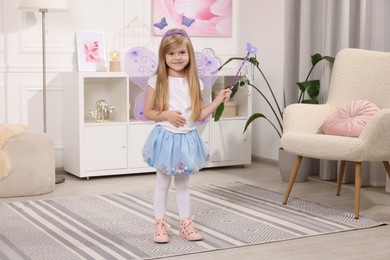 Photo of Cute little girl in fairy costume with violet wings and magic wand at home