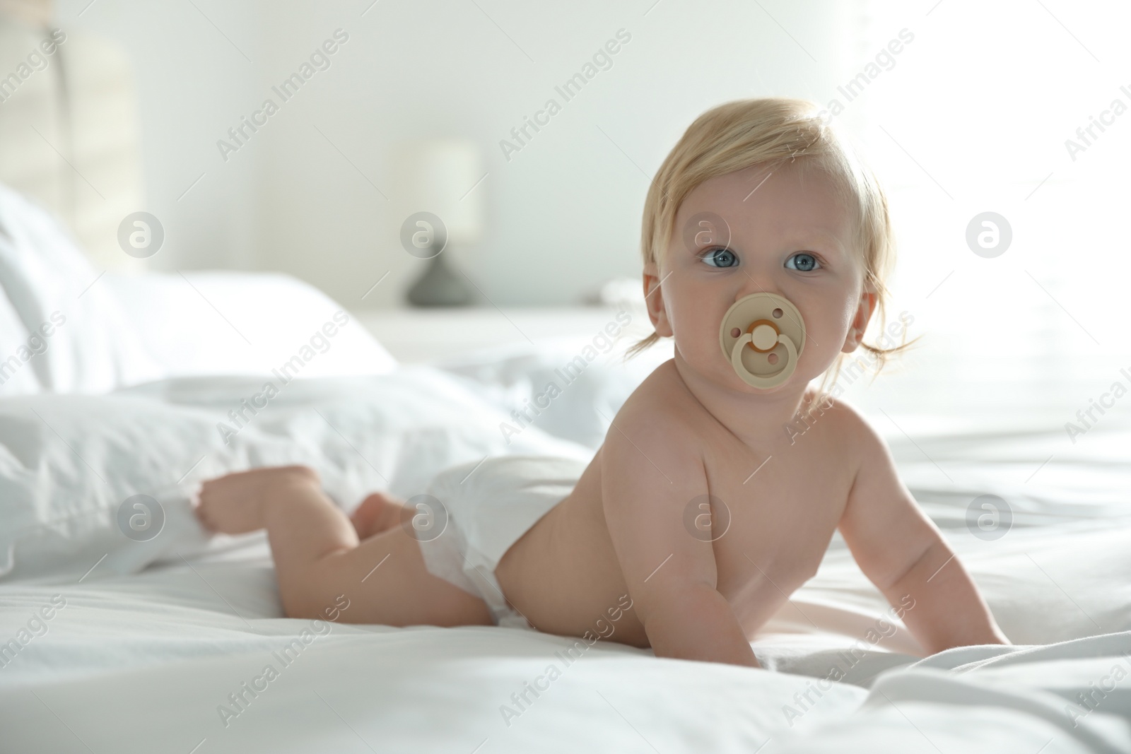 Photo of Cute little baby in diaper with pacifier lying on bed at home