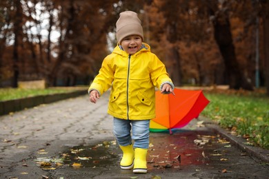 Cute little girl walking in puddle near colorful umbrella outdoors