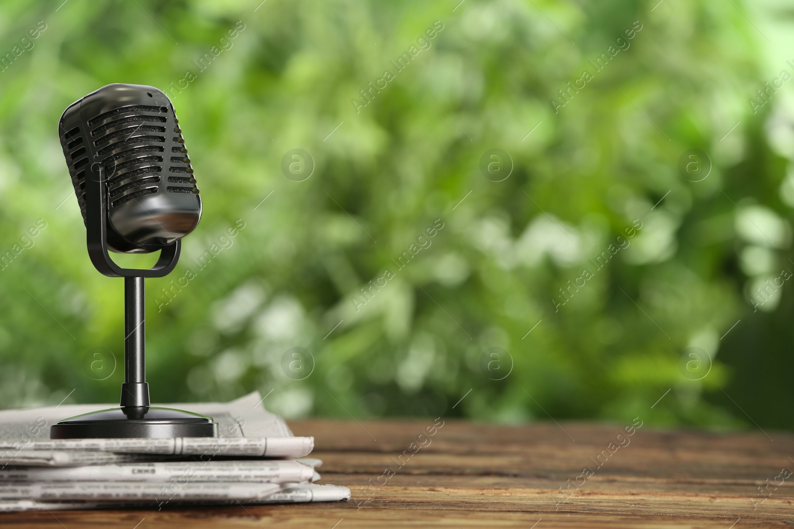 Photo of Newspapers and vintage microphone on wooden table against blurred green background, space for text. Journalist's work