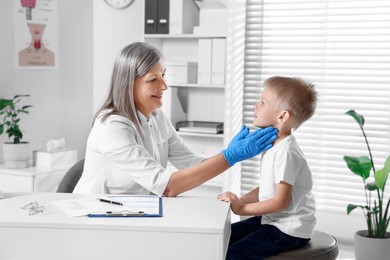 Photo of Endocrinologist examining boy's thyroid gland at table in hospital