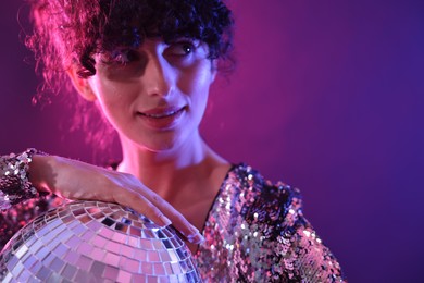 Photo of Beautiful young woman with disco ball posing on color background in neon lights, closeup. Space for text