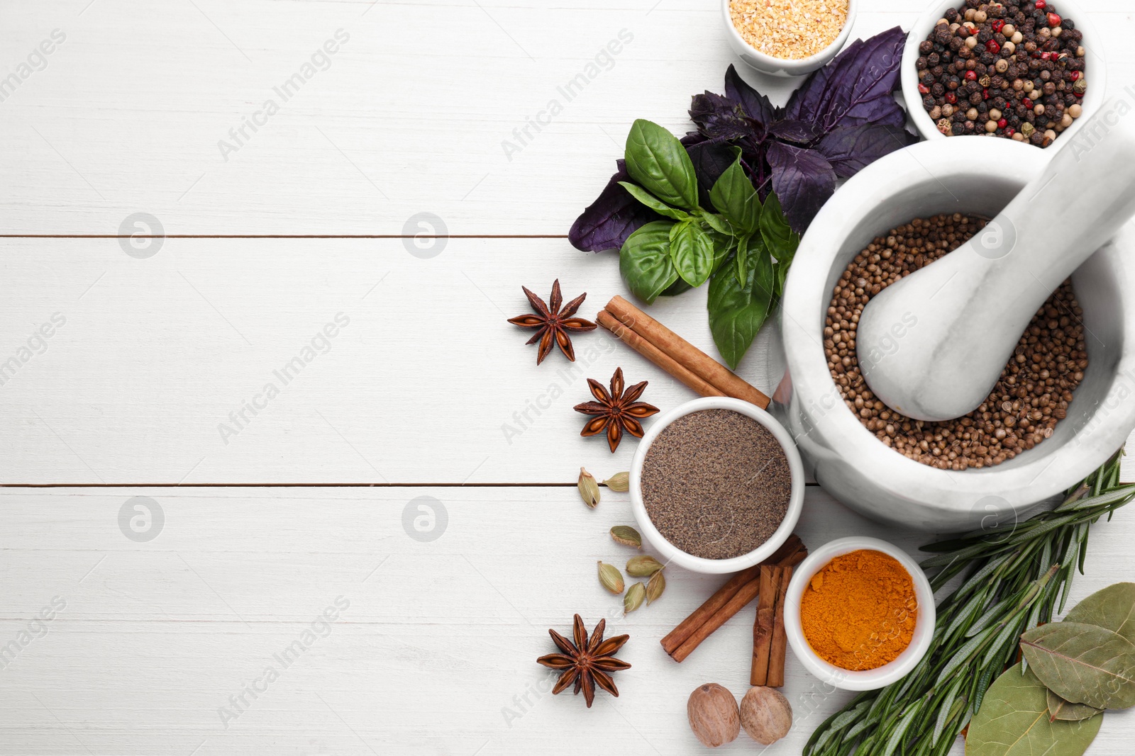 Photo of Mortar with pestle and different spices on white wooden table, flat lay. Space for text