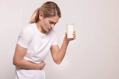 Photo of Woman with glass of milk suffering from lactose intolerance on white background, space for text