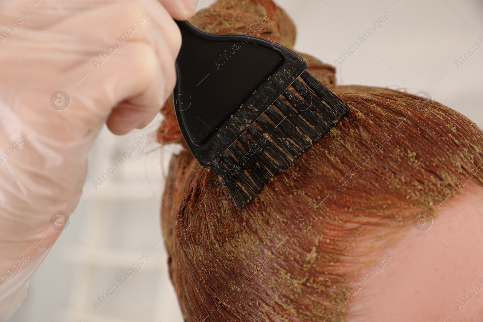 Photo of Young woman dyeing her hair with henna on blurred background, closeup
