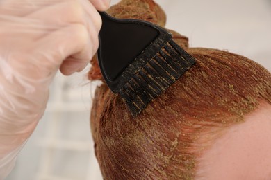 Young woman dyeing her hair with henna on blurred background, closeup