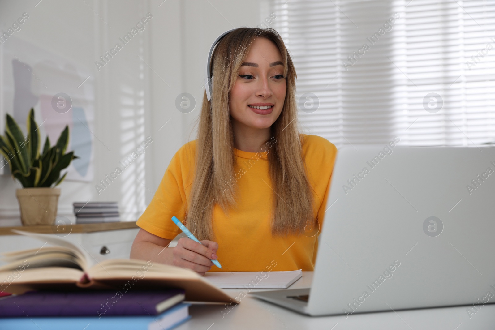 Photo of Young woman watching webinar at table in room