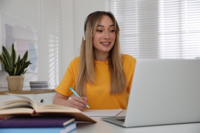 Photo of Young woman watching webinar at table in room