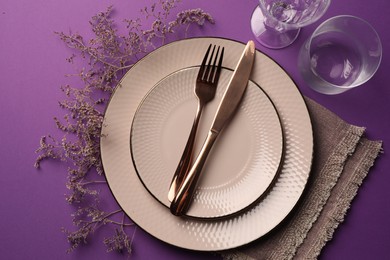 Photo of Stylish table setting. Plates, cutlery, glasses and floral decor on purple background, flat lay